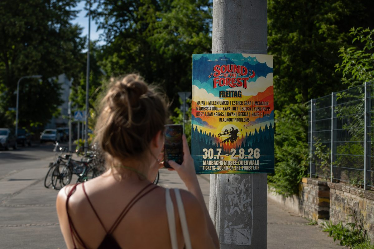 Junge Frau fotografiert ein Veranstaltungs-Plakat an einem Laternenmast